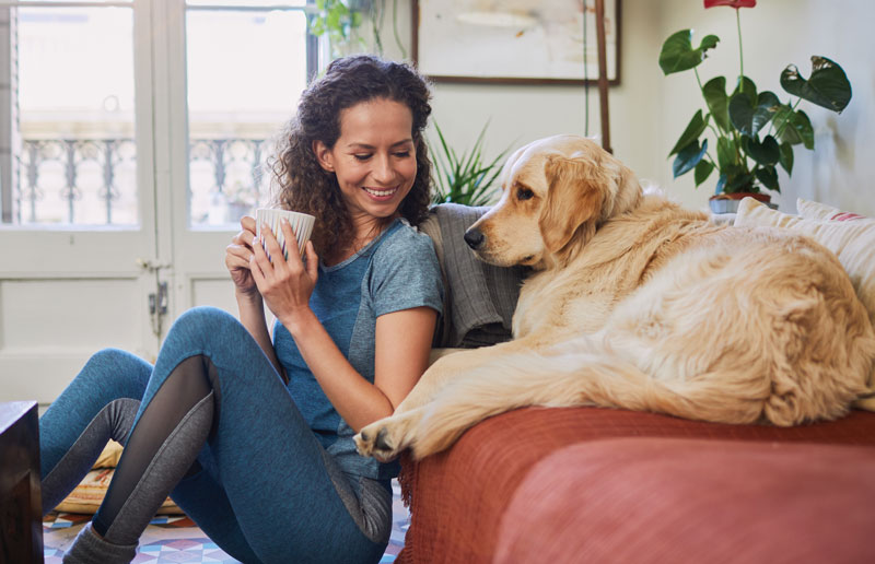 Woman drinking coffee next to a dog on the couch