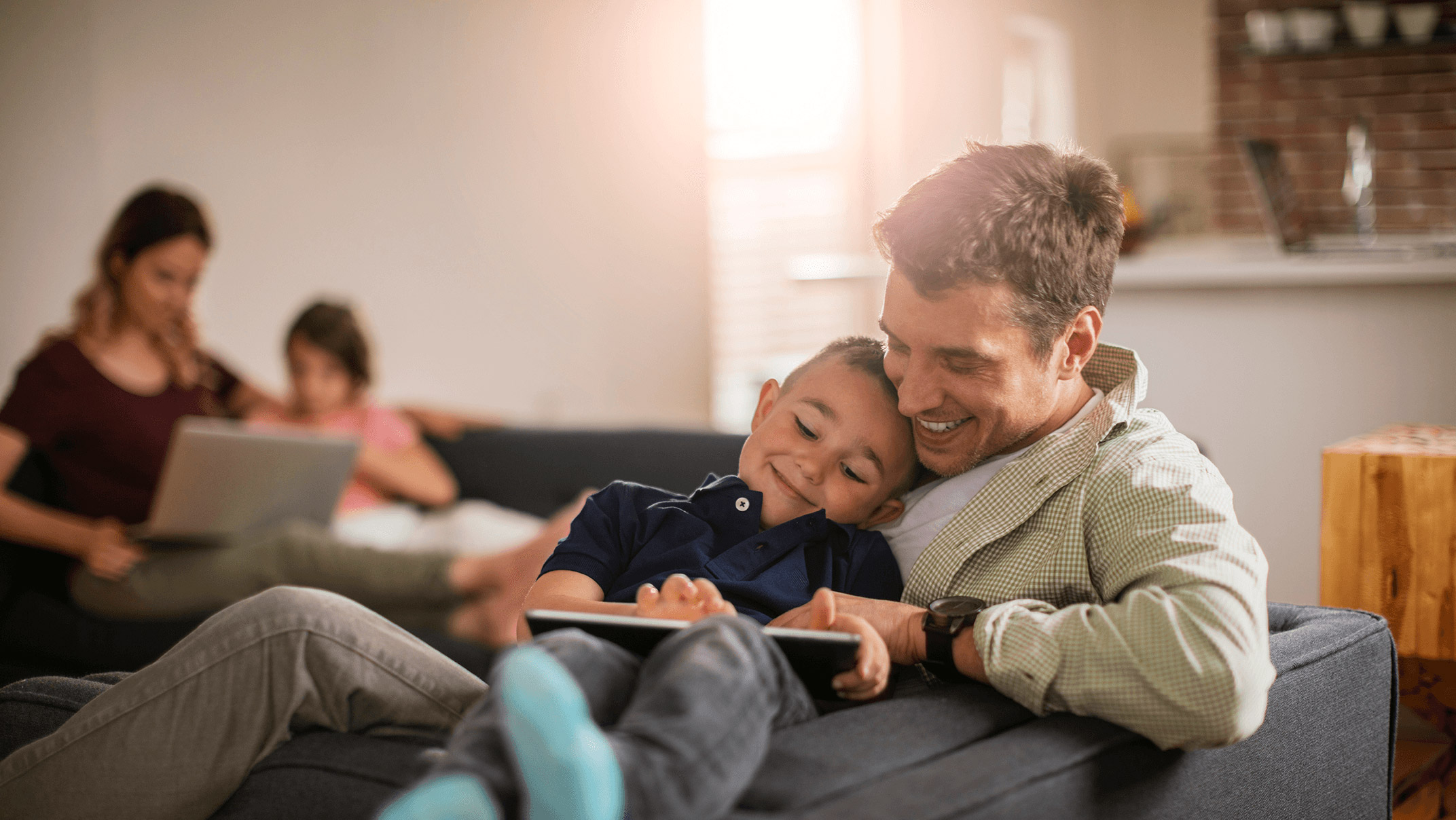 Family relaxing on the couch looking at a tablet and laptop.