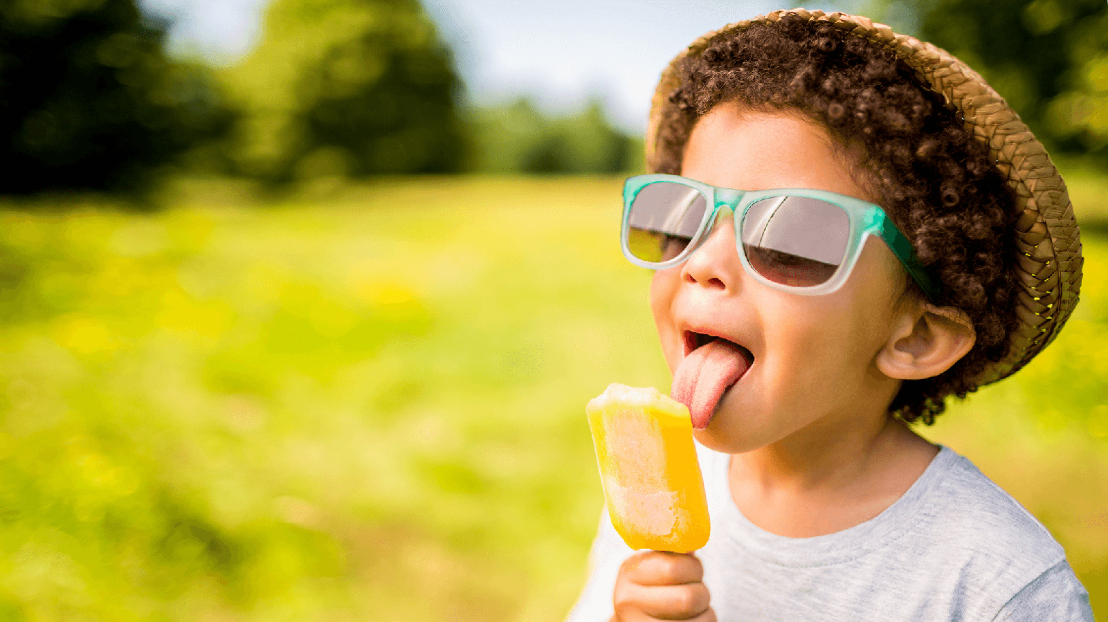 Little boy in grassy field licking a popsicle.