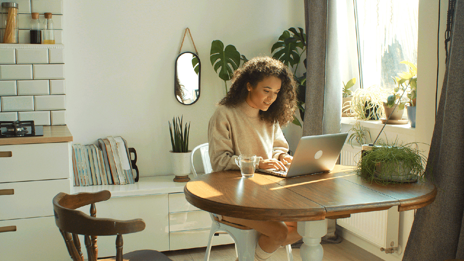 Woman working on a laptop in her sunny kitchen.