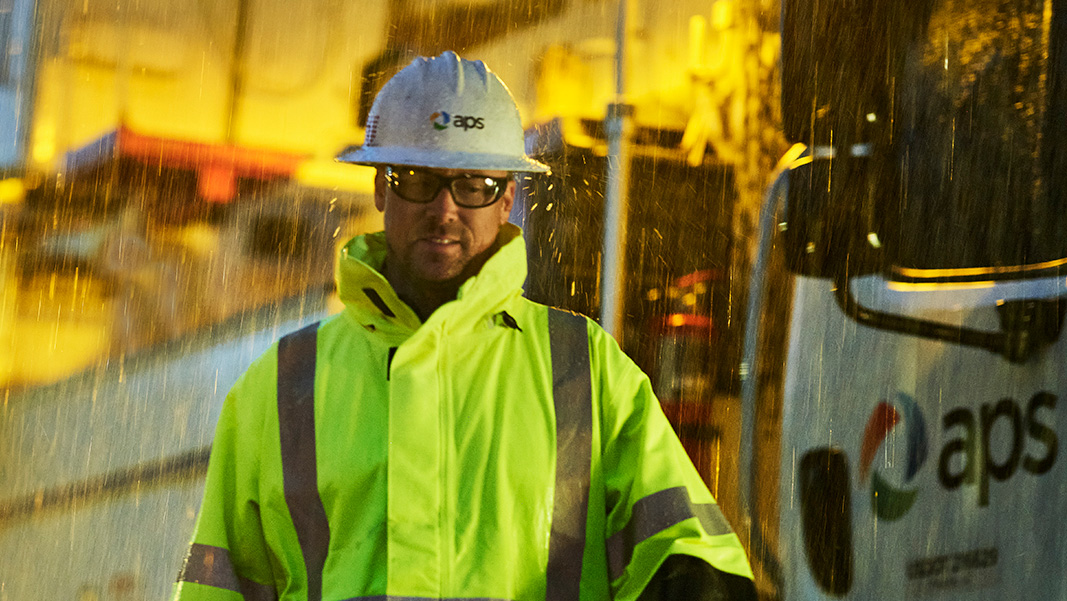 An APS Lineworker in a rain storm, standing beside an APS boom truck