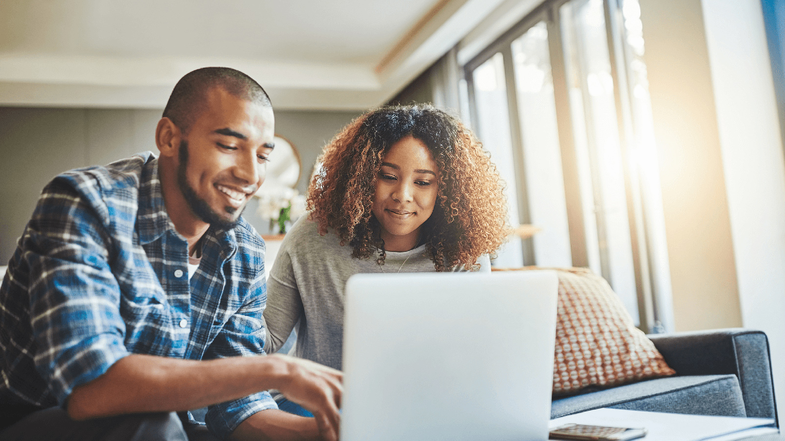 Couple smiling at a laptop in their living room.