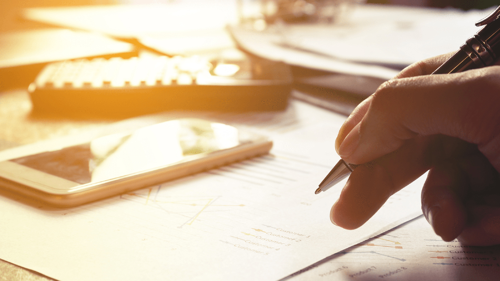 Paperwork, a phone, and a remote spread out on a sunny desk.