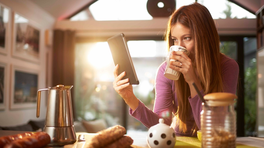 Woman drinking coffee while looking at a tablet 