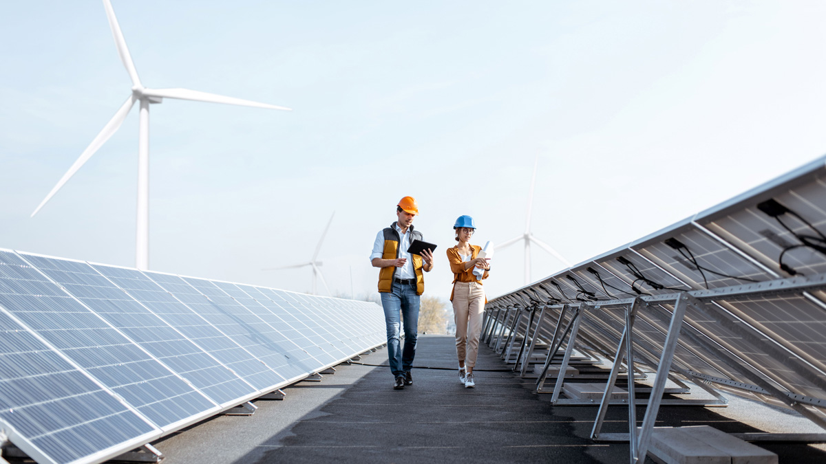 Employees walkling through solar panels with a wind turbine in the background.